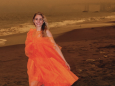 Influencer catches flack for posing in a vibrant orange dress, amid eerily glowing sky, during California fires